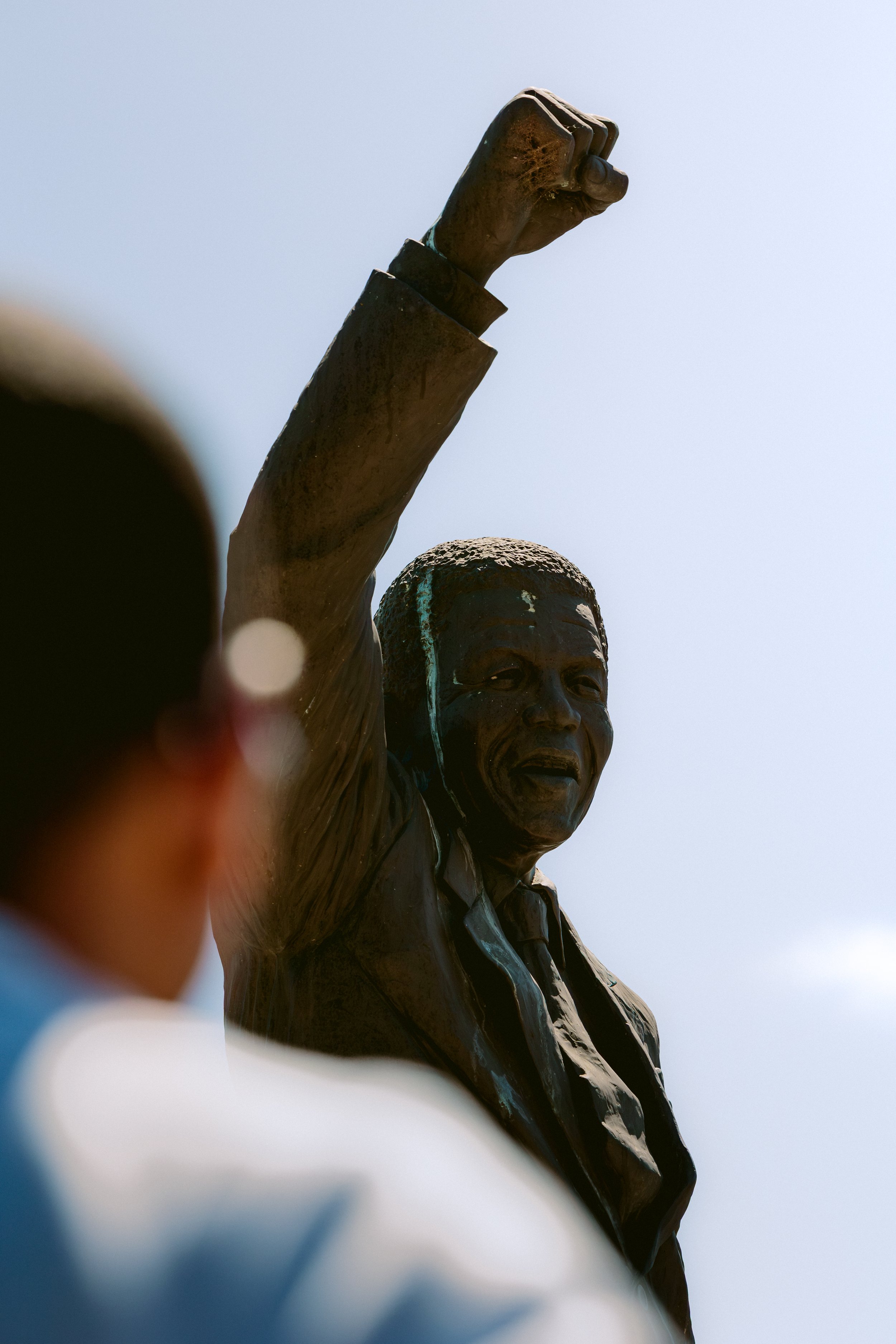 A statue of a suited figure raising a clenched fist, with a person out of focus in the foreground.