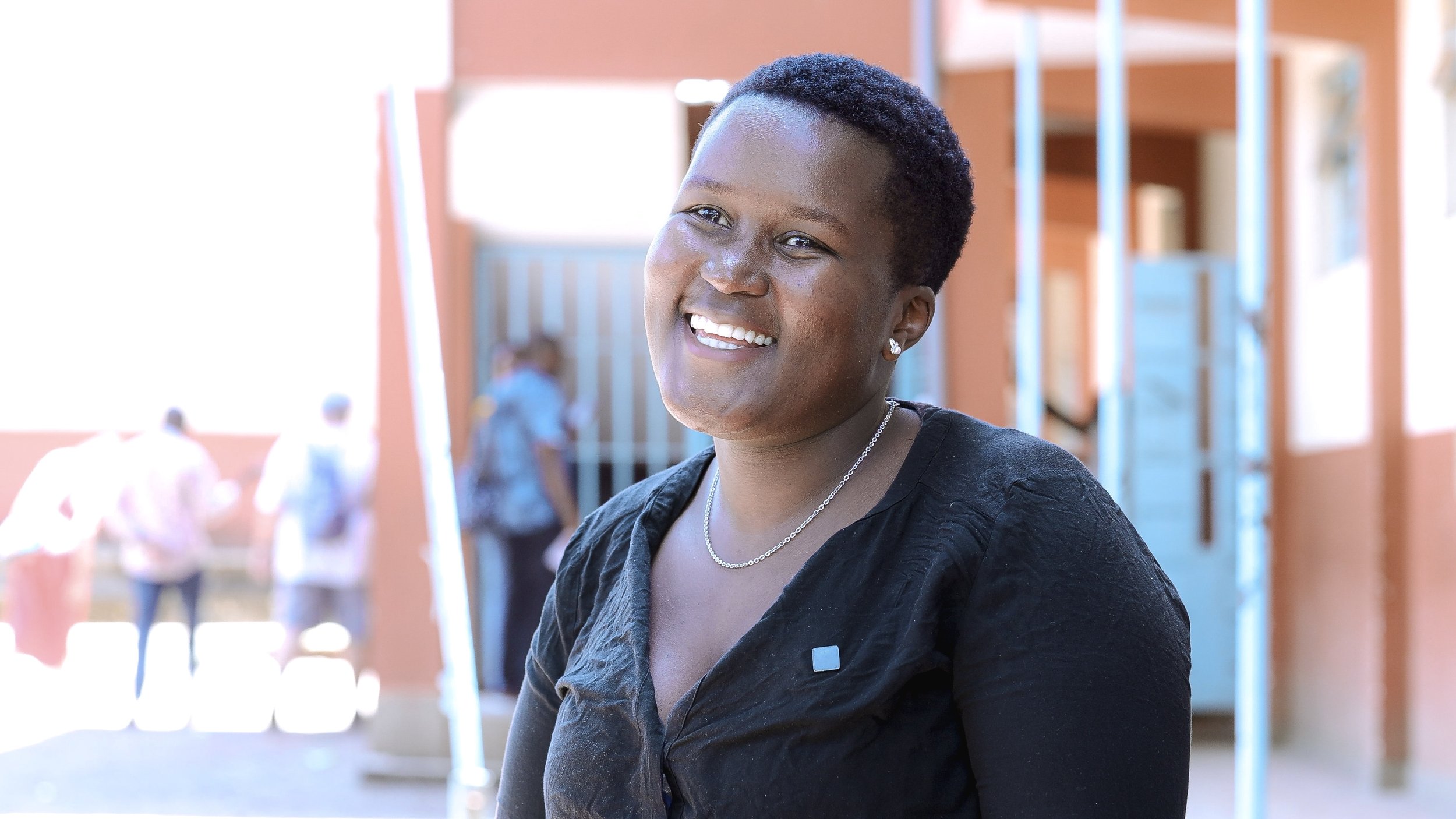 Damackline smiling in a black top in an outdoor corridor.