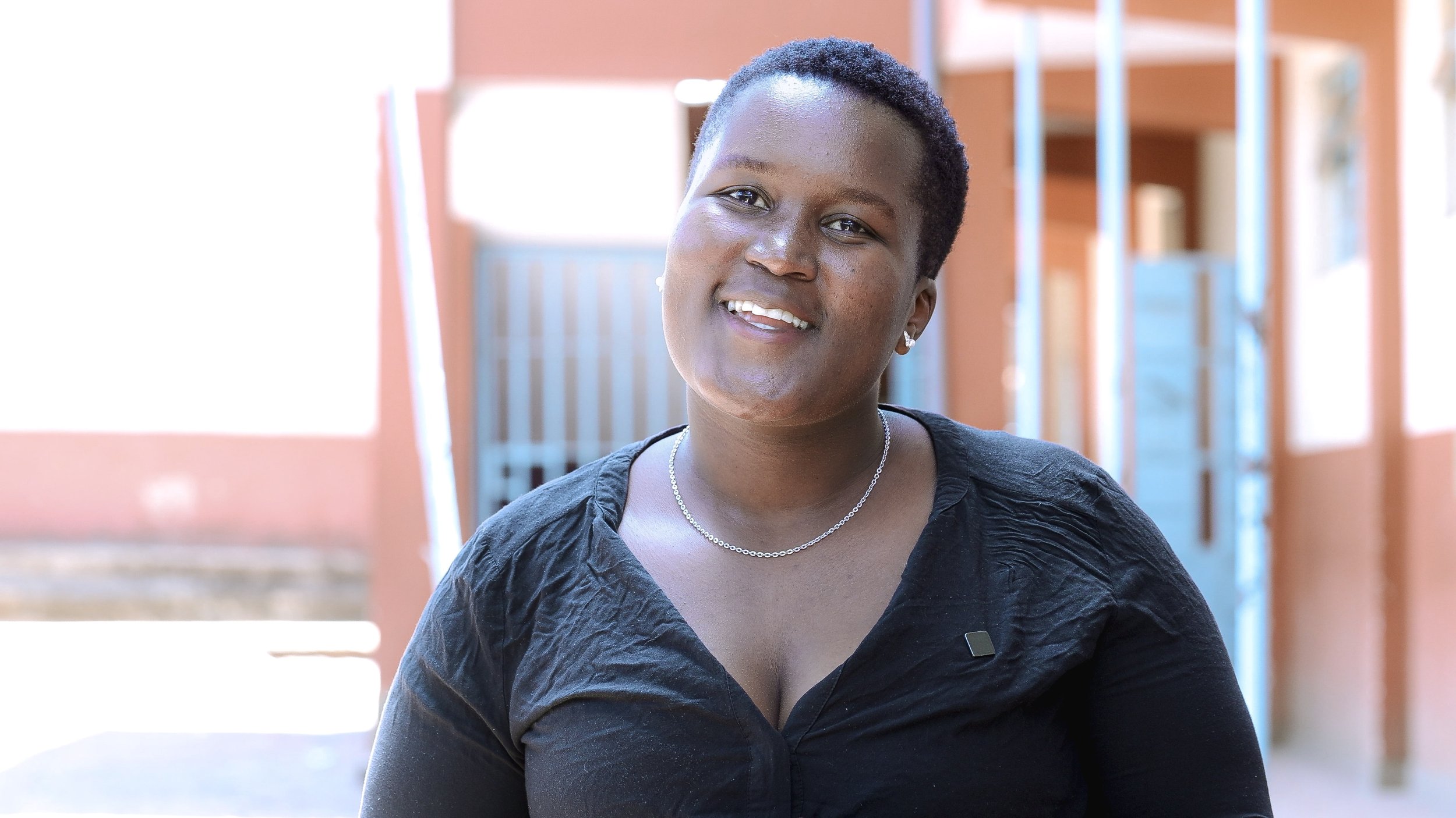 Damackline smiling in a black top in an outdoor corridor.